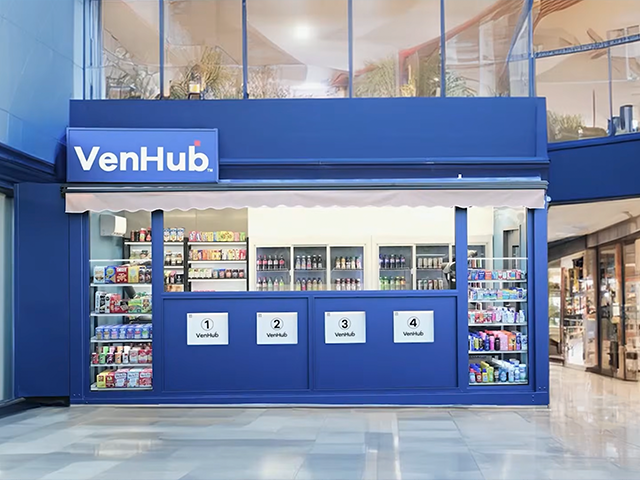 Image showing a blue VenHub unmanned retail kiosk featuring glass display shelves stocked with drinks and snacks with pickup bays numbered 1-4
